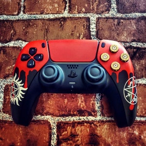 May include: A black and red video game controller with gold accents and a red and black design featuring a pentagram and a symbol of a demon. The controller has a red and black design with a pentagram and a symbol of a demon.