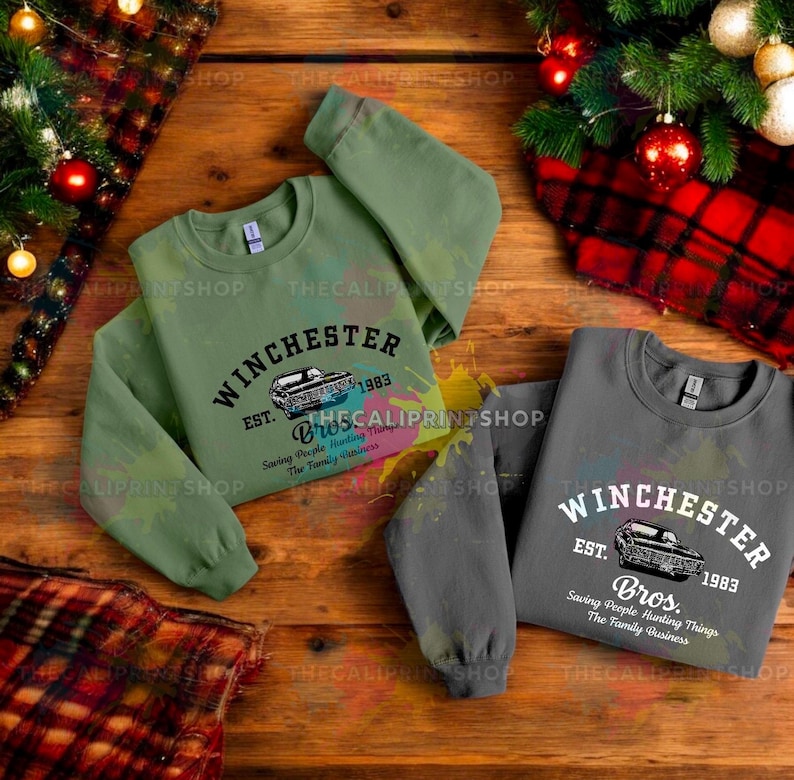 K&ouml;nnte beinhalten: Zwei Sweatshirts mit einem Vintage-Auto-Motiv und dem Text "Winchester Est. 1983 Bros. Saving People Hunting Things The Family Business" bedruckt. Ein Sweatshirt ist gr&uuml;n und das andere ist grau.
