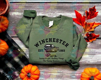 May include: A green sweatshirt with a black graphic print of a car and the text "Winchester Est. 1983 Bros. Saving People Hunting Things The Family Business"