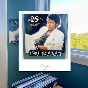 May include: A black vinyl record with a white border and a picture of Michael Jackson on the cover. The record is titled "Thriller" and says "The World's Biggest Selling Album of All Time" on the cover. The record is on a black stand with the words "NOW SPINNING" written in white. The record is in front of a window with a view of trees and a blue sky. The word "Rap" is written in black below the record.