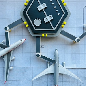 May include: A model airport terminal with two airplanes, one white with red and blue accents and the text "Malaysia" and the other white with red and blue accents and the text "American Airlines", parked at the gates.