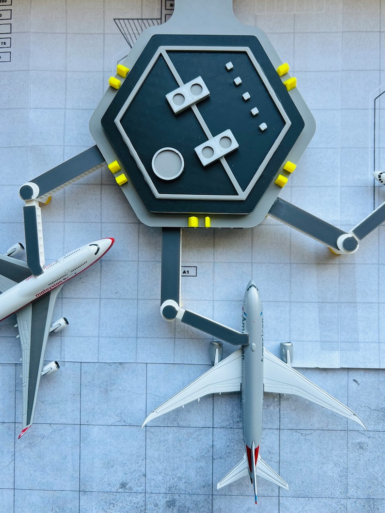 May include: A model airport terminal with two airplanes, one white with red and blue accents and the text "Malaysia" and the other white with red and blue accents and the text "American Airlines", parked at the gates.