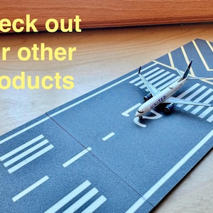 May include: A toy airplane model of a United Airlines plane on a gray and white runway playset. The runway has white lines and yellow markings.