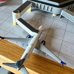 May include: A white and blue airplane model with the word "UNITED" on the side, sitting on a gray and white tiled surface. The airplane is connected to a white and gray gate.