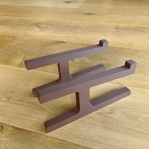 Puede incluir: Un soporte para portátil de metal marrón con un diseño simple y moderno. El soporte está hecho de tres barras horizontales que están conectadas por soportes verticales. El soporte está diseñado para elevar un portátil a una altura de visualización más ergonómica.