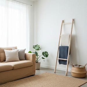 Può includere: Un accogliente soggiorno con un divano beige, un tappeto in iuta e una scala in legno per coperte. Due coperte, una color crema e una blu navy, sono appese alla scala. Una pianta in vaso e un cestino in vimini completano l'arredamento. Il tappeto misura circa 150 cm x 200 cm.