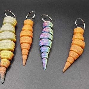 May include: Four colorful keychains shaped like a spiral. The keychains are made of plastic and have a silver metal ring. The colors are yellow, orange, blue, and purple.
