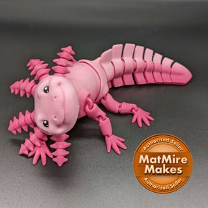 May include: A pink articulated axolotl toy with a segmented tail and a friendly face. The toy is made of plastic and has a textured surface.