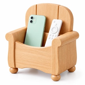 May include: A light-colored wooden organizer shaped like a miniature armchair with four small ball feet. The organizer holds a light green smartphone and a white remote control in its central compartment, featuring a curved backrest and armrests.