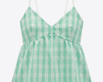 Peut inclure: Un haut caraco sans manches avec un motif à carreaux vert menthe clair et blanc. Le vêtement présente une encolure en V, une couture à la taille empire froncée et de fines bretelles réglables, créant une silhouette évasée type péplum.