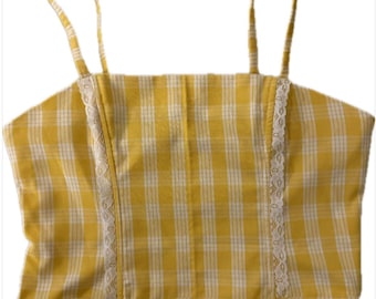 Peut inclure: Haut court à carreaux jaunes et blancs avec fines bretelles. Le haut présente une encolure carrée et est bordé de dentelle blanche sur les côtés. Le tissu a un motif quadrillé.