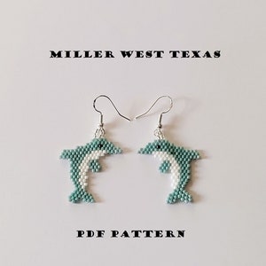 Könnte beinhalten: Ein Paar Perlen-Delfin-Ohrringe mit silbernen Haken. Die Delfine sind hellblau und weiß mit schwarzen Augen. Die Ohrringe sind mit "MILLER WEST TEXAS PDF PATTERN" beschriftet.