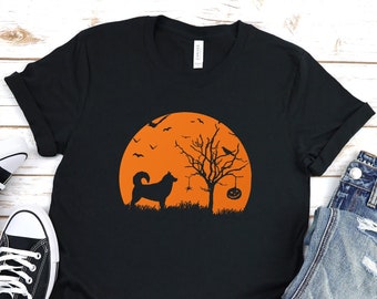 May include: Black t-shirt with a Halloween-themed graphic. The design features a silhouette of a dog, a tree, and a pumpkin against an orange sunset. The word "BLACK" is printed at the bottom. Includes black canvas sneakers and blue jeans.