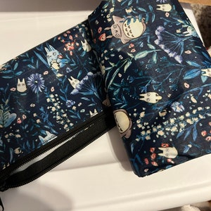 May include: Two blue reusable shopping bags with a floral pattern and cartoon characters. The bags are folded and have a zipper closure.