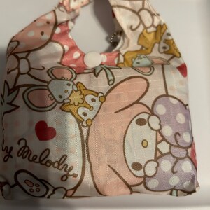 May include: A pink and white reusable shopping bag featuring a My Melody character design. The bag has a pink and white polka dot pattern and a white button closure.