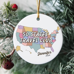May include: A white ceramic ornament with a colorful map of the United States. The ornament reads "50 States Travel Club" and is personalized with the name "Jennifer" and the year "2024".