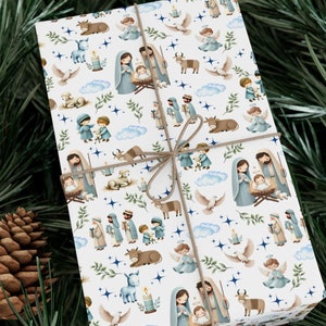 May include: White wrapping paper with a repeating pattern of a nativity scene with blue, white, and gold accents. The pattern includes stars, angels, and animals.