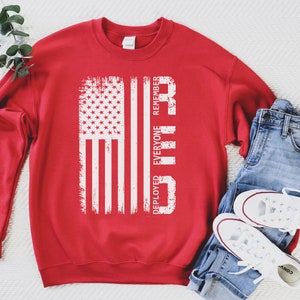 May include: Red sweatshirt with a white distressed American flag and the text "Deployed Everyone Remember" printed on the front.