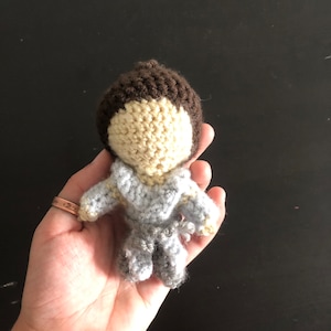 May include: A crocheted doll with brown hair, a light blue and cream colored outfit, and a light blue scarf.