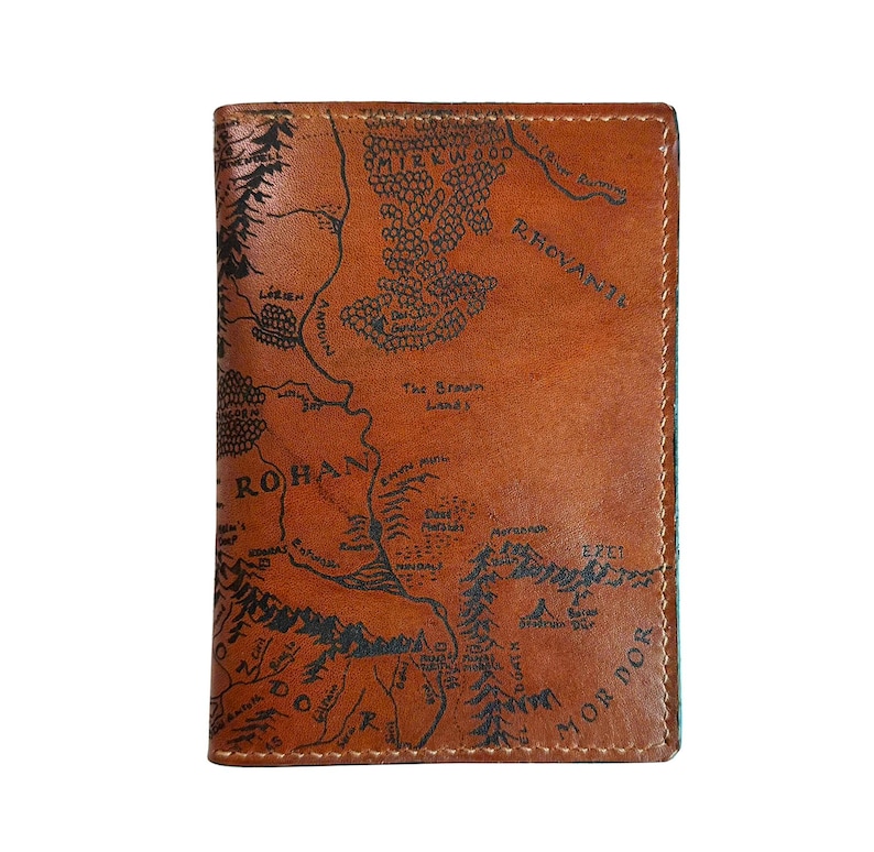 May include: A brown leather wallet featuring a detailed map design. The map includes text such as "Rohan" and "Mordor", with intricate illustrations of mountains and forests. The wallet is rectangular and appears to be new.