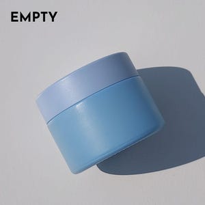 May include: A small, round, blue cosmetic jar with a light blue lid. The word "EMPTY" is printed in black at the top. The jar casts a shadow on a white surface.