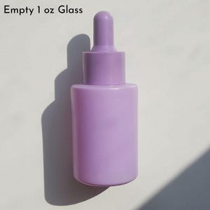 May include: A lavender-colored glass dropper bottle, labeled "Empty 1 oz Glass." The bottle has a cylindrical body and a rounded top with a dropper. The bottle is designed for dispensing liquids.