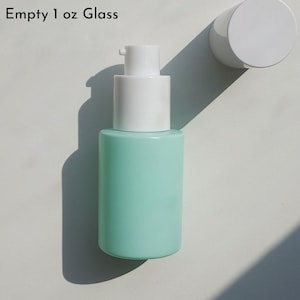 May include: A light teal 1 oz glass bottle with a white pump dispenser and a white cap. The bottle is cylindrical and has the text "Empty 1 oz Glass" printed on the top left.