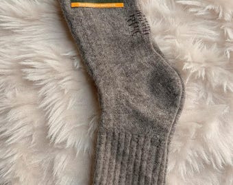 May include: A single gray sock with a ribbed cuff and a tag that reads "YANMAL". The tag features a landscape image. The sock is made of a soft, textured material, likely wool, and is designed for warmth and comfort.