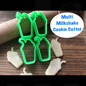 May include: Green plastic cookie cutter shaped like a milkshake. The cutter is shown on a wooden surface with several cookies cut out using the cutter.