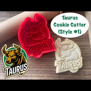 May include: Red plastic Taurus cookie cutter with a bull's head design. The cutter is next to a beige cookie with the same design. The cookie cutter and cookie both have the word "Taurus" written on them.