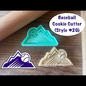 Puede incluir: Tres cortadores de galletas de béisbol con forma de montaña con una pelota de béisbol. Uno es verde azulado, otro morado y blanco, y otro beige. El texto "Baseball Cookie Cutter (Style #20)" está en un óvalo blanco.
