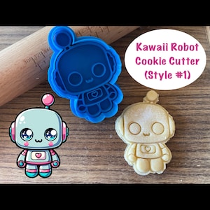 May include: Blue plastic cookie cutter shaped like a kawaii robot with a pink heart on its chest. A cookie cut with the cutter is shown next to it.