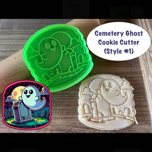 May include: Green plastic cookie cutter shaped like a ghost in a graveyard. The ghost is smiling and has a tombstone behind it. The cookie cutter is on a wooden surface. Cemetery Ghost Cookie Cutter (Style #1)