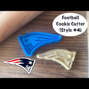 May include: A blue plastic football cookie cutter in the shape of a team logo, next to a baked cookie in the same shape. The text "Football Cookie Cutter (Style #4)" is in a white oval.