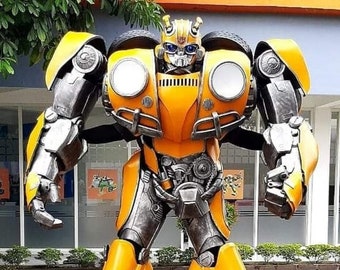 May include: A yellow and silver robot with a car-like design. The robot has large round headlights and a black grill. The robot is standing on a brick walkway.