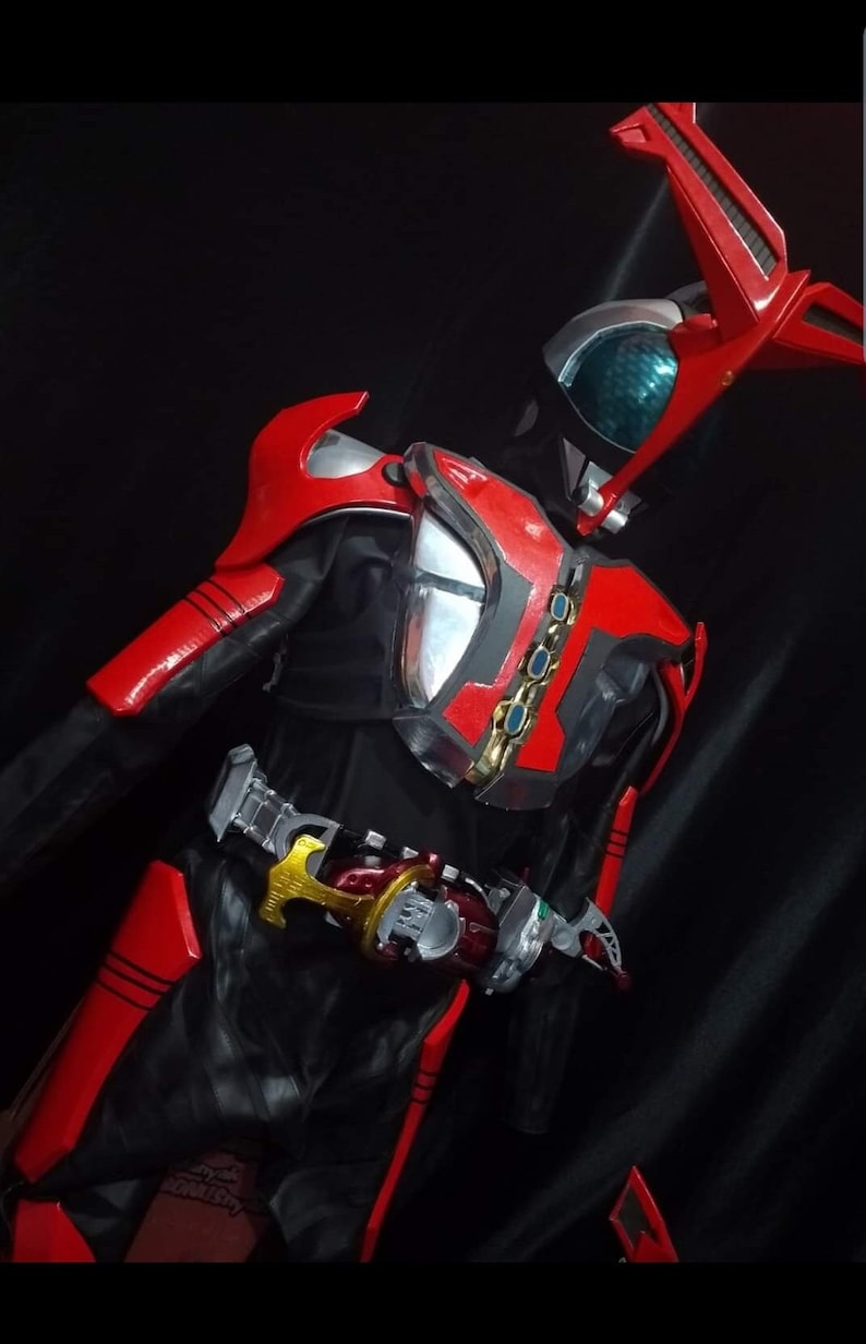 May include: A red and black action figure with a silver chest plate and a red helmet with a green visor. The figure is wearing a black belt with a gold buckle and a red and black cape.