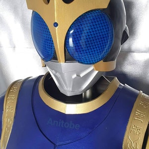 K&ouml;nnte beinhalten: Ein blaues und goldenes Superhelden-Kost&uuml;m mit einem Helm, der eine schwarze Gesichtsmaske und blaue Augen hat. Der Helm hat zwei goldene H&ouml;rner oben. Das Kost&uuml;m hat goldene Akzente und einen goldenen Saum um den Hals.