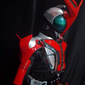 May include: A red and silver action figure with a black helmet and a green visor. The figure has a large red wing on its back and a silver belt with a buckle.