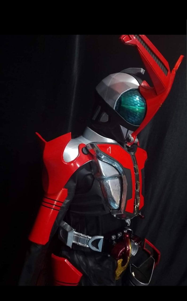 May include: A red and silver action figure with a black helmet and a green visor. The figure has a large red wing on its back and a silver belt with a buckle.