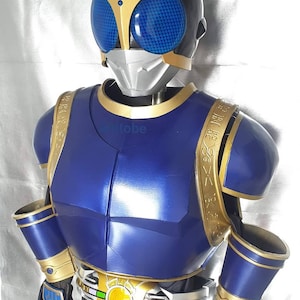 K&ouml;nnte beinhalten: Ein blaues und goldenes Superhelden-Kost&uuml;m mit einem Helm, der eine blaue Visier und goldene Akzente aufweist. Das Kost&uuml;m hat einen G&uuml;rtel mit einer goldenen Schnalle und einem gelben Kreis in der Mitte.
