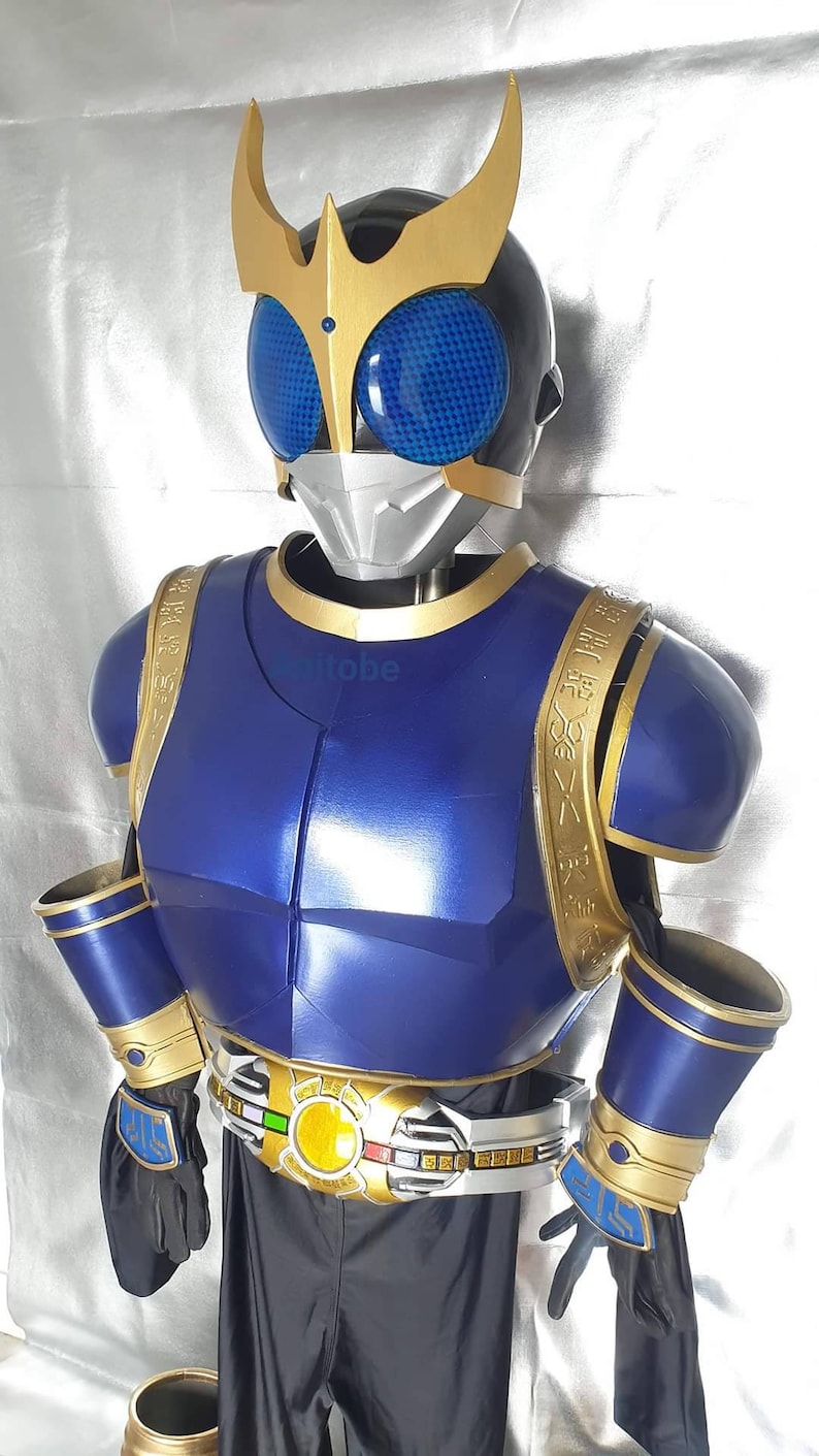 K&ouml;nnte beinhalten: Ein blaues und goldenes Superhelden-Kost&uuml;m mit einem Helm, der eine blaue Visier und goldene Akzente aufweist. Das Kost&uuml;m hat einen G&uuml;rtel mit einer goldenen Schnalle und einem gelben Kreis in der Mitte.