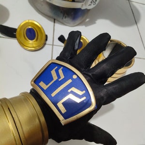 K&ouml;nnte beinhalten: Ein schwarzer Lederhandschuh mit einem goldenen und blauen Emblem, auf dem "ZII" steht. Der Handschuh wird an der linken Hand einer Person getragen.