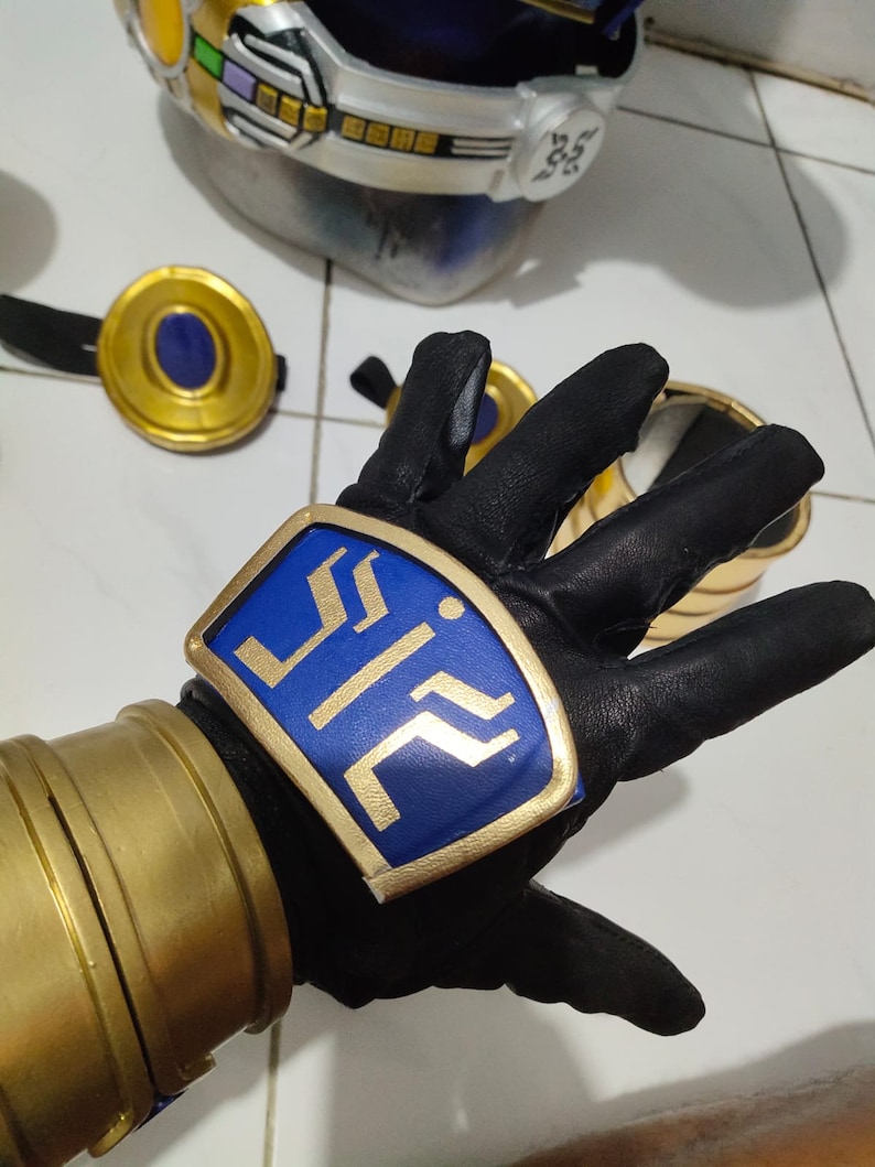 K&ouml;nnte beinhalten: Ein schwarzer Lederhandschuh mit einem goldenen und blauen Emblem, auf dem "ZII" steht. Der Handschuh wird an der linken Hand einer Person getragen.