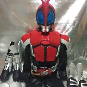 May include: A red and silver Kamen Rider costume with a black belt and a red helmet with blue eyes. The costume includes a chest piece, shoulder pads, gloves, and boots.