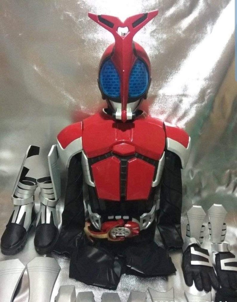 May include: A red and silver Kamen Rider costume with a black belt and a red helmet with blue eyes. The costume includes a chest piece, shoulder pads, gloves, and boots.