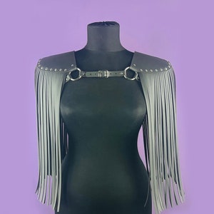 Puede incluir: Pieza de hombro de cuero gris con flecos y detalles plateados. La pieza de hombro está en un maniquí.