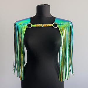 Puede incluir: Hombrera con flecos verdes y dorados iridiscentes, con una correa con hebilla y anillos y tachuelas de metal plateado. La hombrera se exhibe en un maniquí negro, mostrando su diseño y textura.