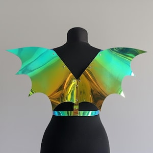May include: Iridescent bat-wing chest piece with a metallic sheen. The wings are a blend of green, gold, and blue. The piece has a V-neck design and a waist strap. Fastened with small rivets and a buckle.