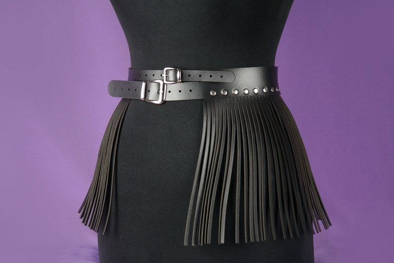 May include: A black leather belt with a fringe skirt attached. The belt has two silver buckles and silver studs.