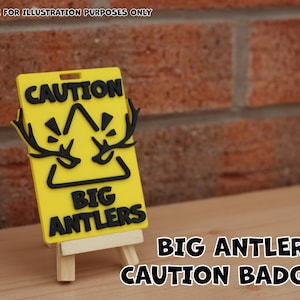Puede incluir: Una placa de precaución amarilla con texto negro y un diseño de cuernos de ciervo. La placa dice "CAUTION BIG ANTLERS" y se muestra en un pequeño caballete de madera. Las palabras "IMAGE FOR ILLUSTRATION PURPOSES ONLY" están en la parte superior.